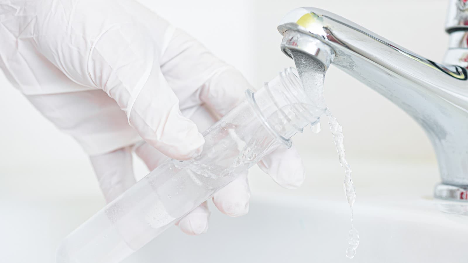 Homeowner collecting a water sample for testing from a kitchen faucet